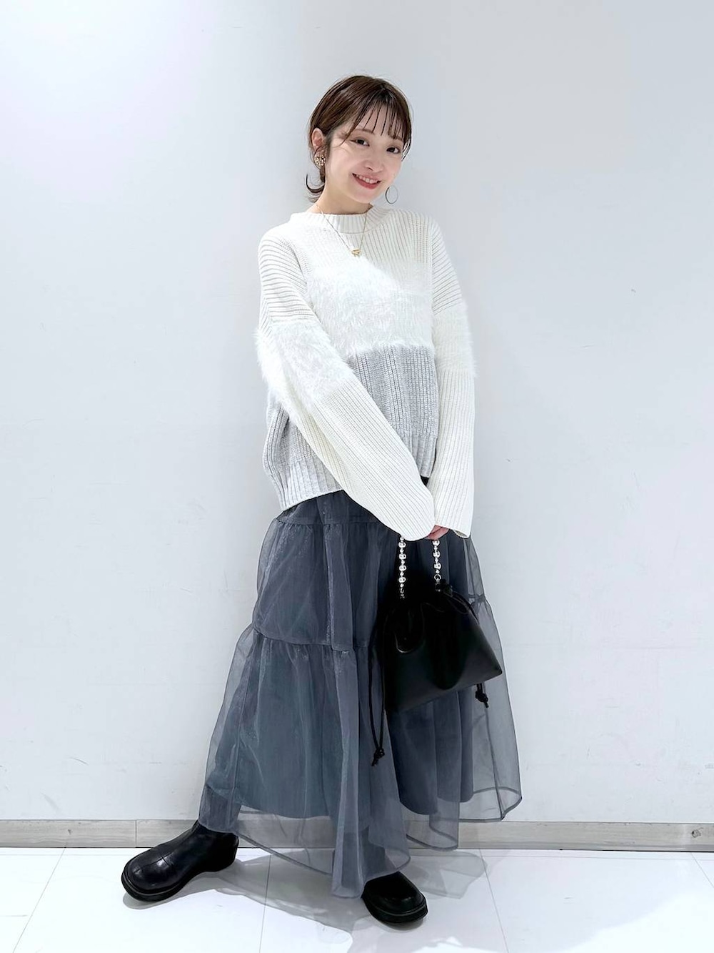 ブラック系のブーツ、ホワイト系のニット/セーター、グレー系のスカートを着用したレディースの冬コーディネートの2枚目の写真