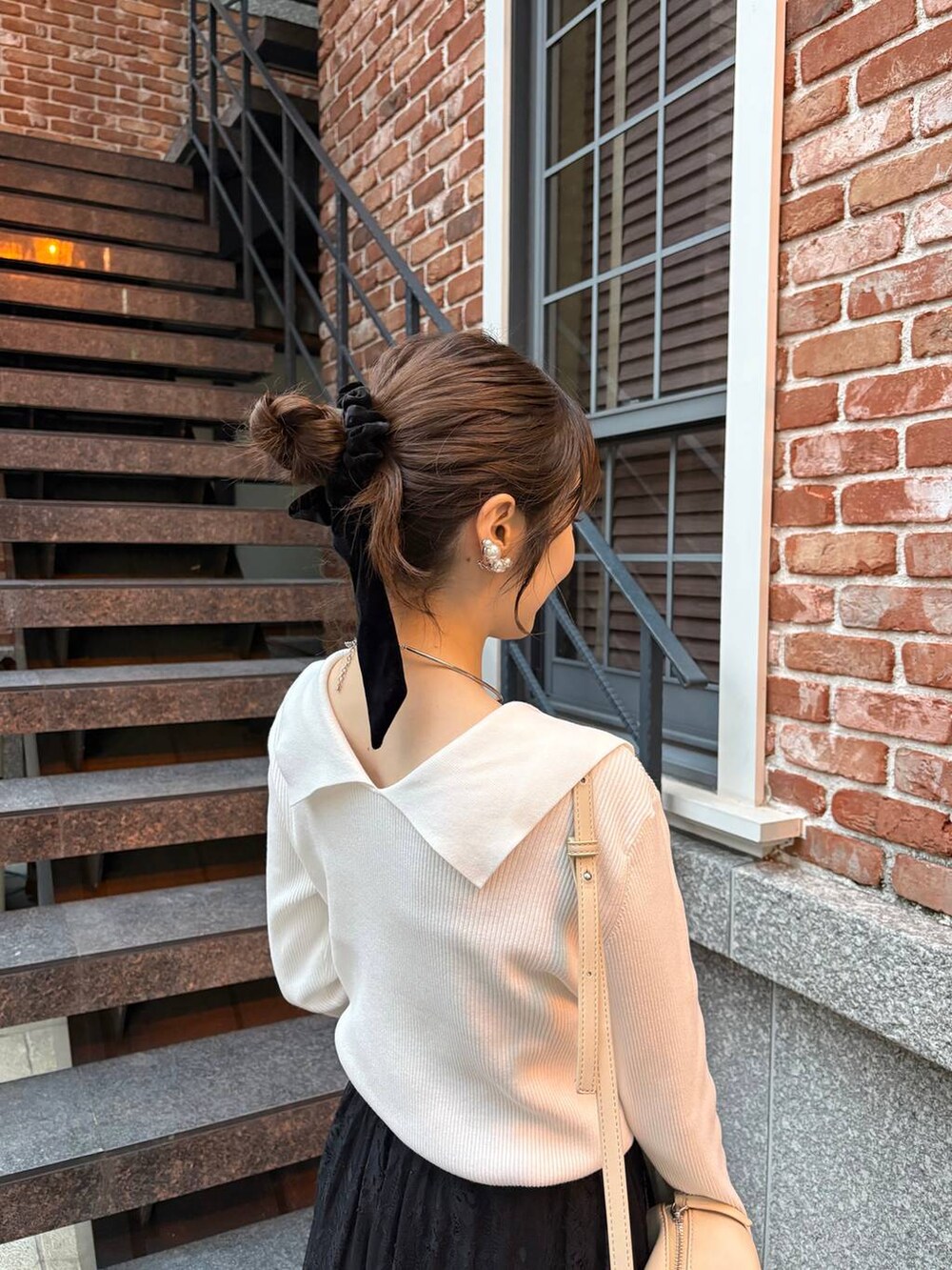 ベージュ系のハンドバッグ、ホワイト系のニット/セーター、シルバー系のチョーカーを着用したレディースの秋コーディネートの2枚目の写真