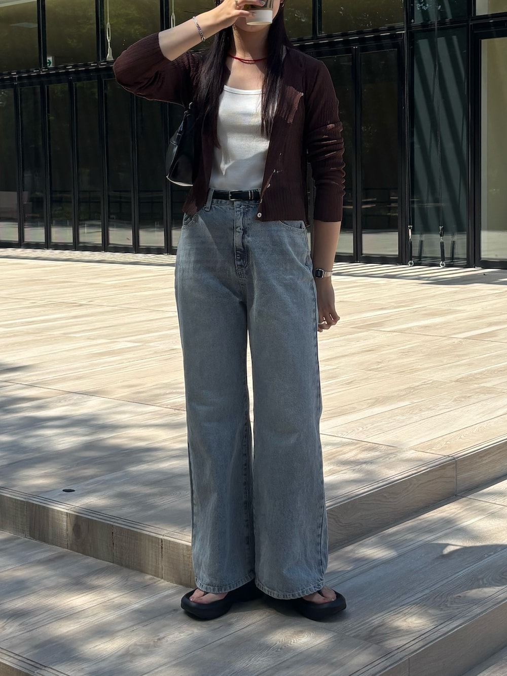 ブルー系のデニムパンツ、ブラック系のハンドバッグ、ブラウン系のカーディガン/ボレロを着用したレディースの夏コーディネートの2枚目の写真