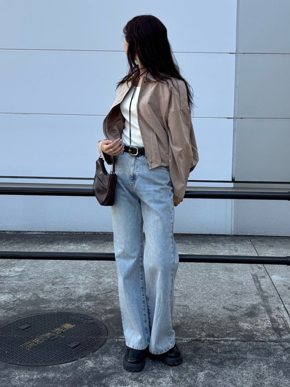 ベージュ系のブルゾン、ブラウン系のハンドバッグ、ブルー系のデニムパンツを着用したレディースの春コーディネートの2枚目の写真