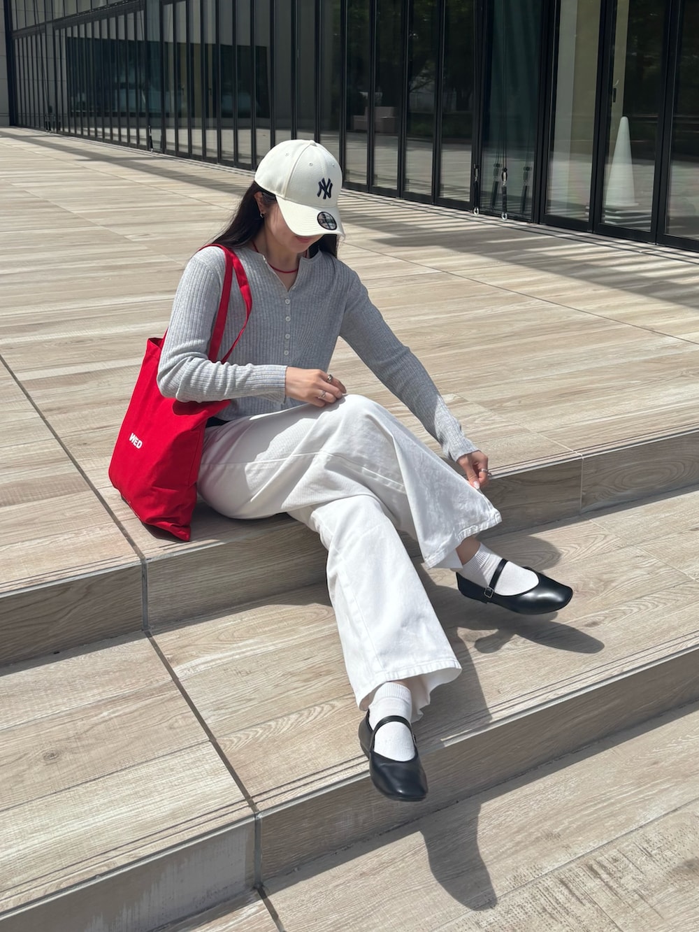 グレー系のカーディガン/ボレロ、レッド系のトートバッグ、ホワイト系のデニムパンツを着用したレディースの春コーディネートの2枚目の写真