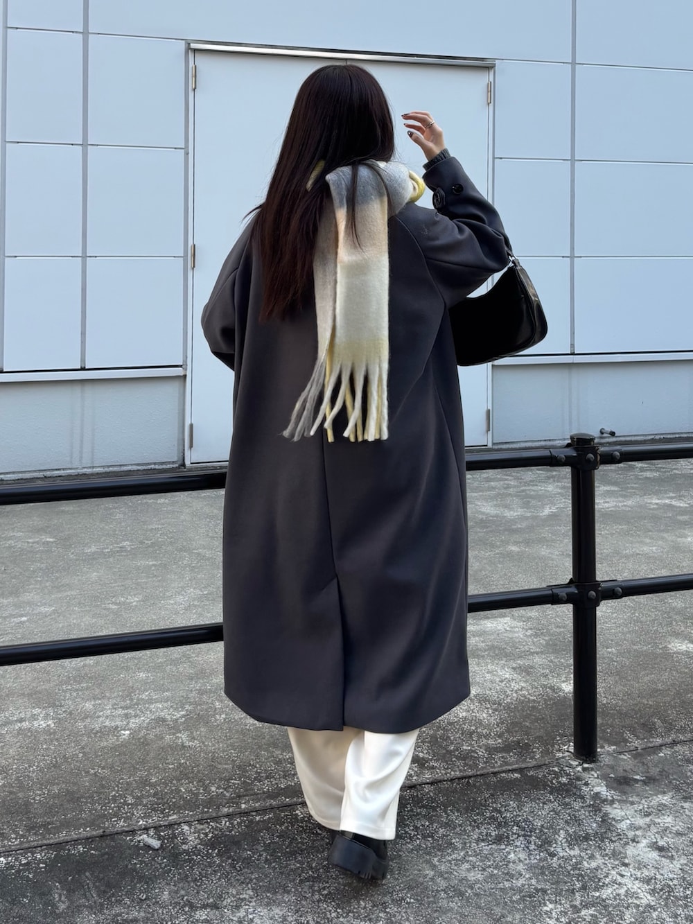 グレー系のステンカラーコート、ホワイト系のスラックス、ブラック系のハンドバッグを着用したレディースの冬コーディネートの3枚目の写真