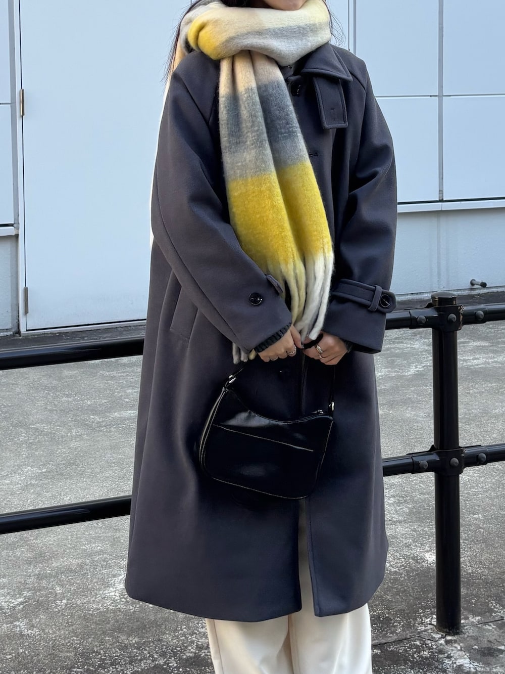 グレー系のステンカラーコート、ホワイト系のスラックス、ブラック系のハンドバッグを着用したレディースの冬コーディネートの2枚目の写真