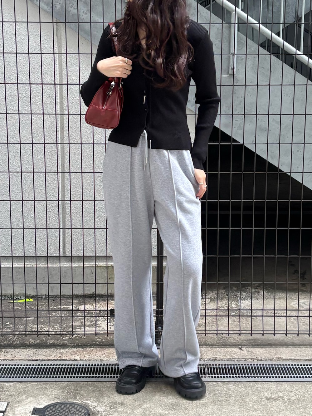 レッド系のボストンバッグ、グレー系のスウェットパンツ、ブラック系のカーディガン/ボレロを着用したレディースの春コーディネートの2枚目の写真