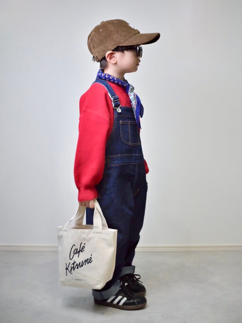 レッド系のニット/セーター、ブルー系のサロペット/オーバーオール、ブラック系のスニーカーを着用したキッズの秋コーディネートの2枚目の写真