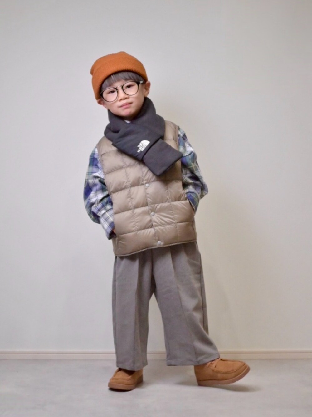 ベージュ系のダウンベスト、グレー系のスラックス、ベージュ系のブーツを着用したキッズの秋コーディネートの3枚目の写真