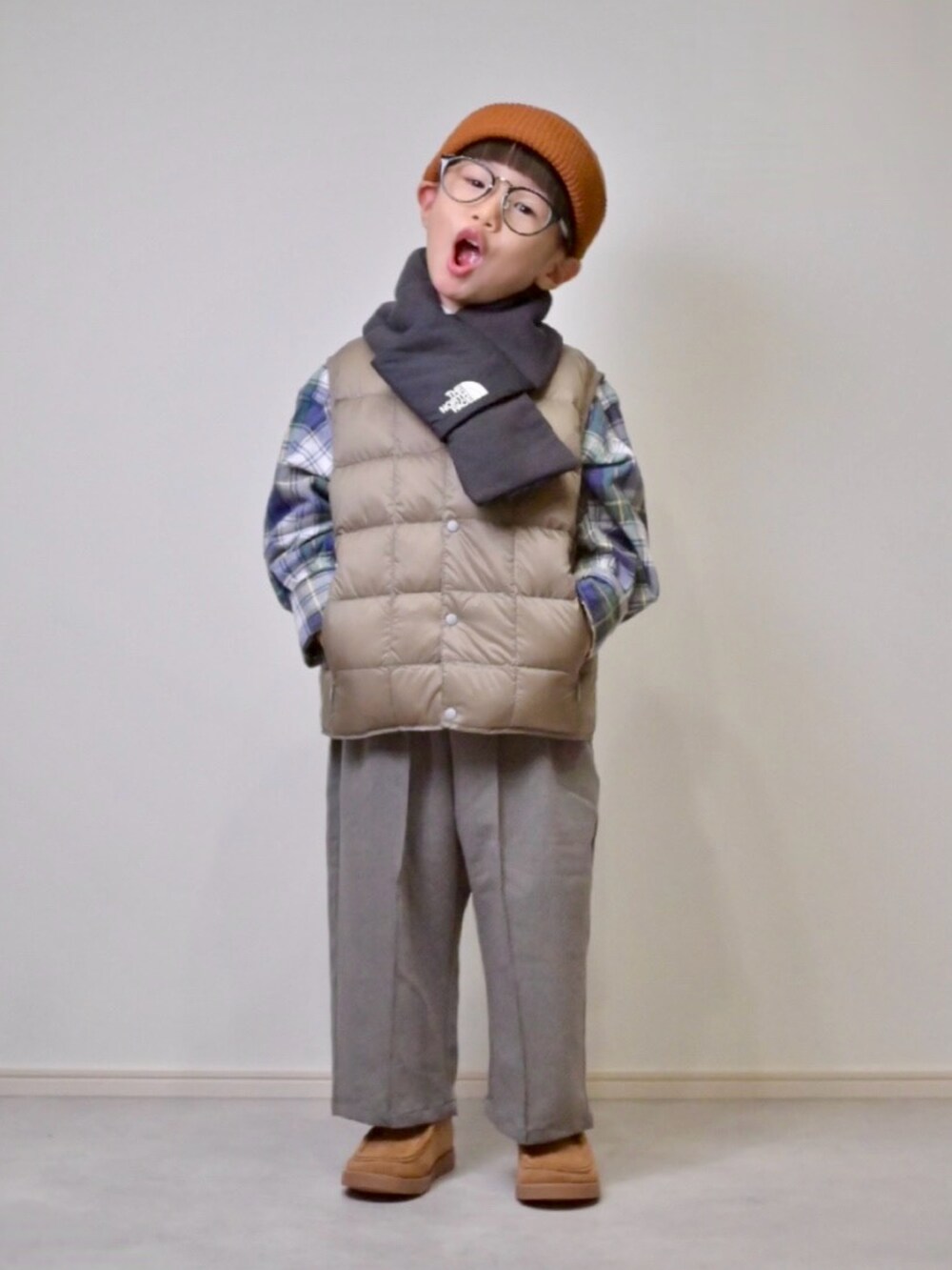 ベージュ系のダウンベスト、グレー系のスラックス、ベージュ系のブーツを着用したキッズの秋コーディネートの4枚目の写真