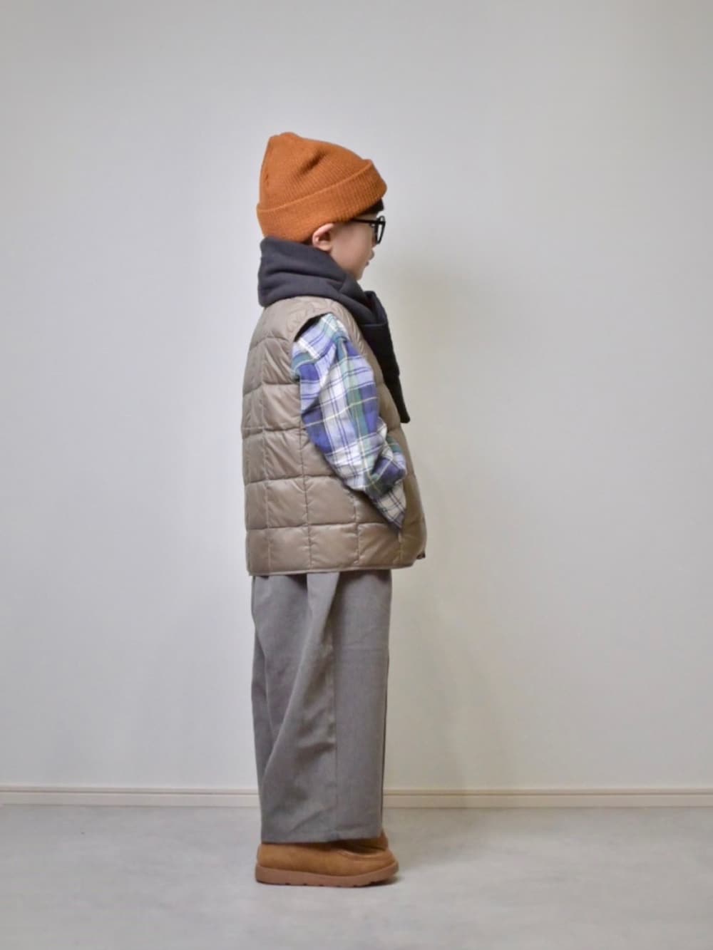 ベージュ系のダウンベスト、グレー系のスラックス、ベージュ系のブーツを着用したキッズの秋コーディネートの2枚目の写真