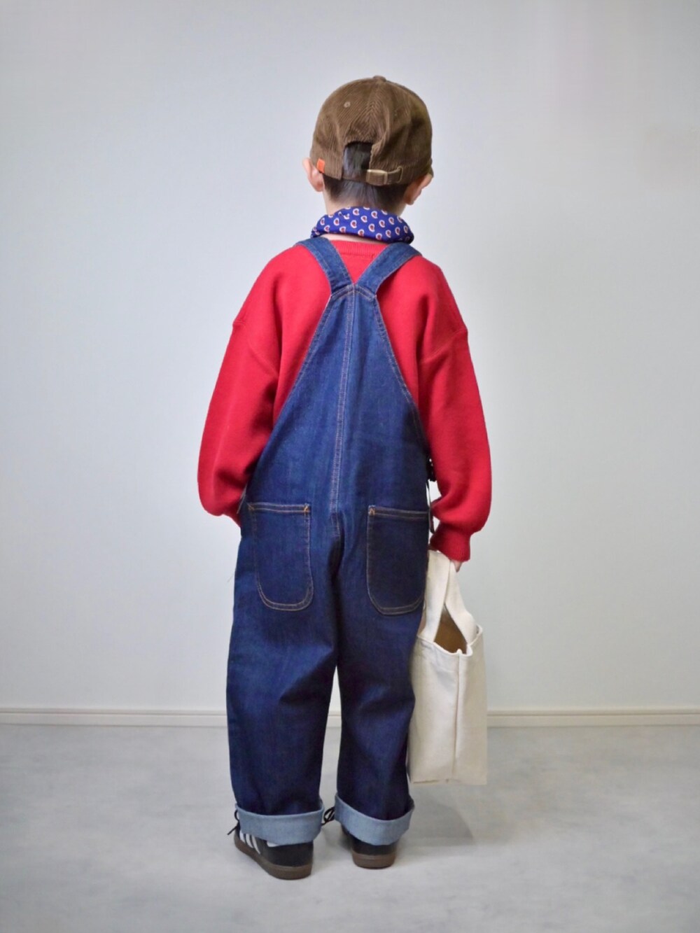 レッド系のニット/セーター、ブルー系のサロペット/オーバーオール、ブラック系のスニーカーを着用したキッズの秋コーディネートの4枚目の写真