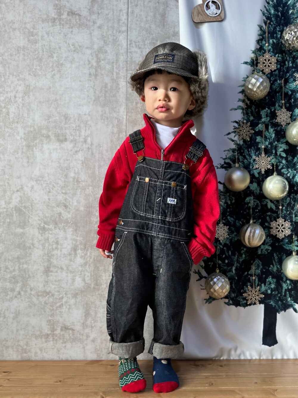 レッド系のニット/セーター、ホワイト系のトップス、ブルー系のサロペット/オーバーオールを着用したキッズの冬コーディネートの2枚目の写真