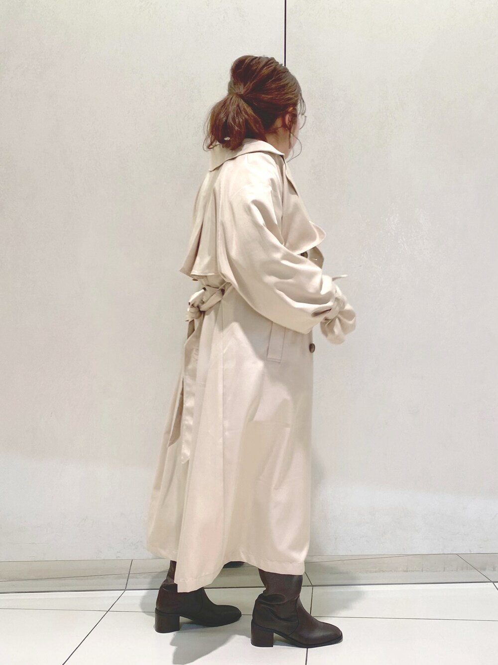 ベージュ系のトレンチコート、ブルー系のTシャツ/カットソー、ブラウン系のブーツを着用したレディースの冬コーディネートの2枚目の写真