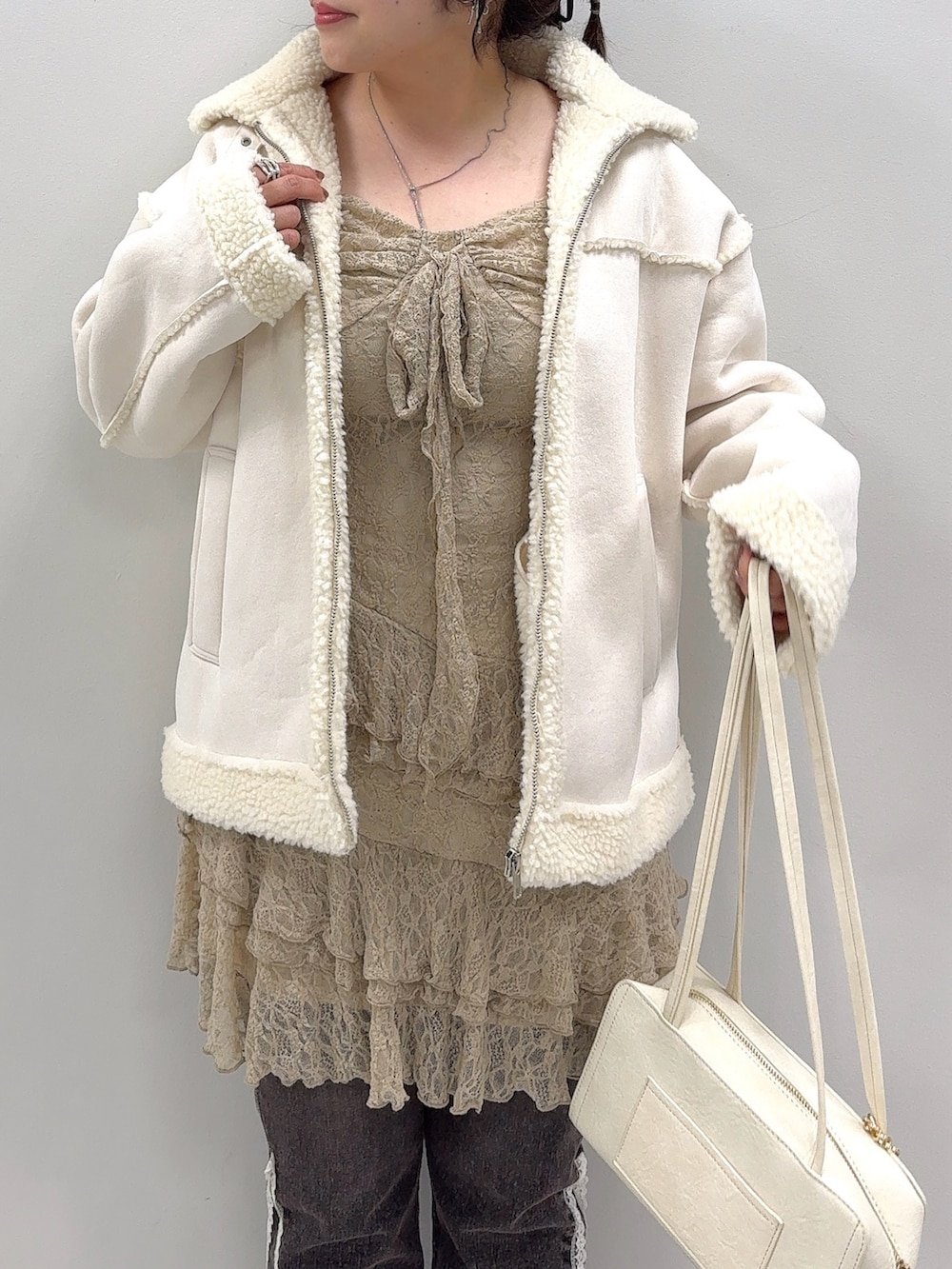 ホワイト系のブルゾン、ベージュ系のワンピース、ブラック系のデニムパンツを着用したレディースの秋コーディネートの4枚目の写真