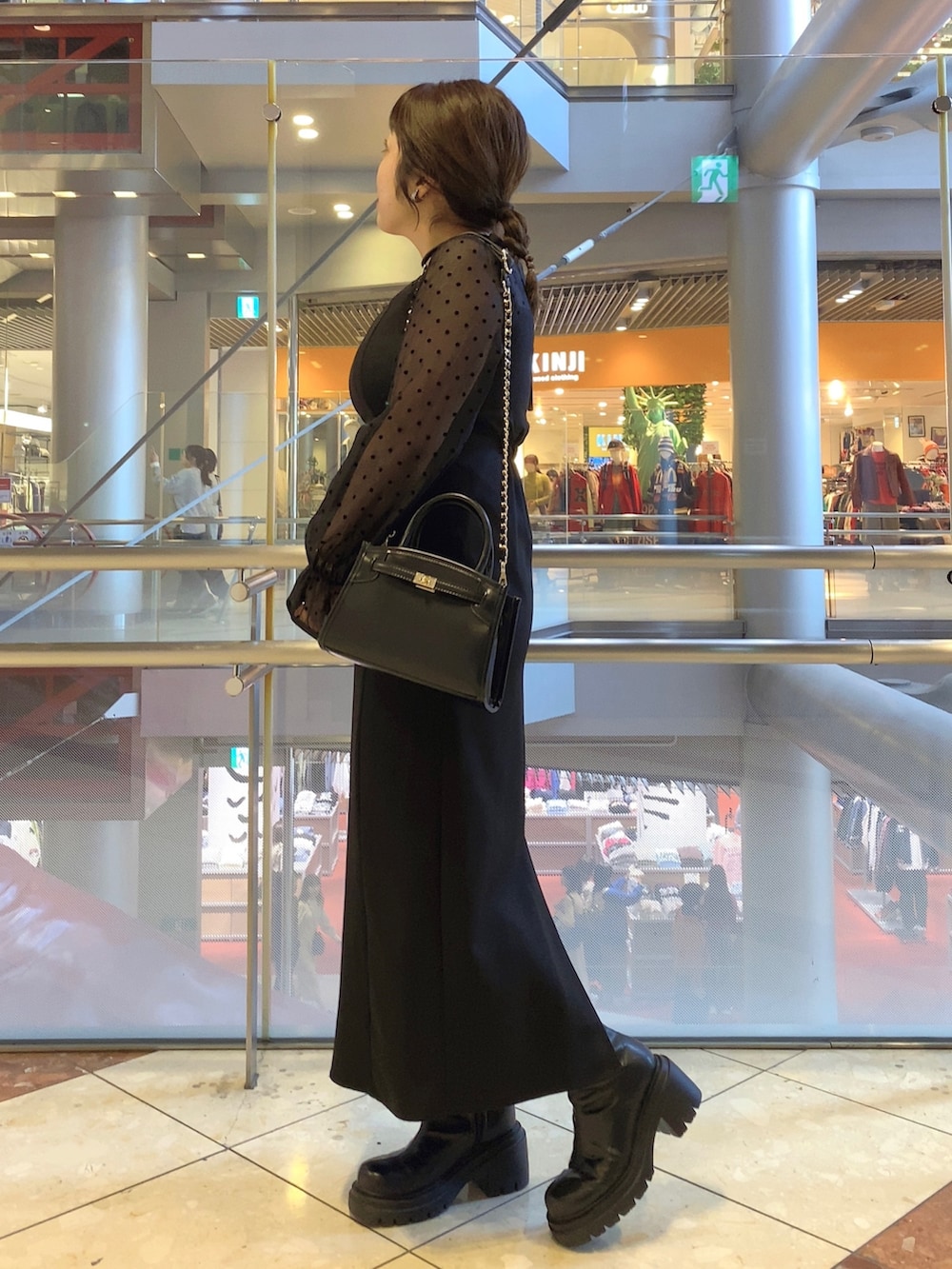 ブラック系のドレス、ブラック系のショルダーバッグ、ブラック系のブーツを着用したレディースの秋コーディネートの3枚目の写真