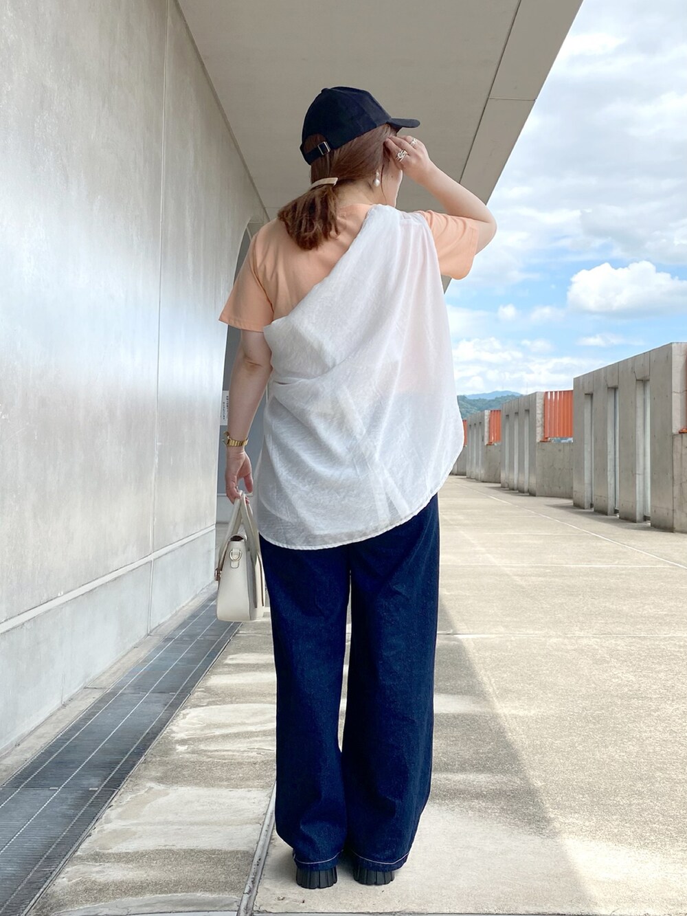 オレンジ系のTシャツ/カットソー、ホワイト系のショルダーバッグ、ブルー系のデニムパンツを着用したレディースの夏コーディネートの4枚目の写真