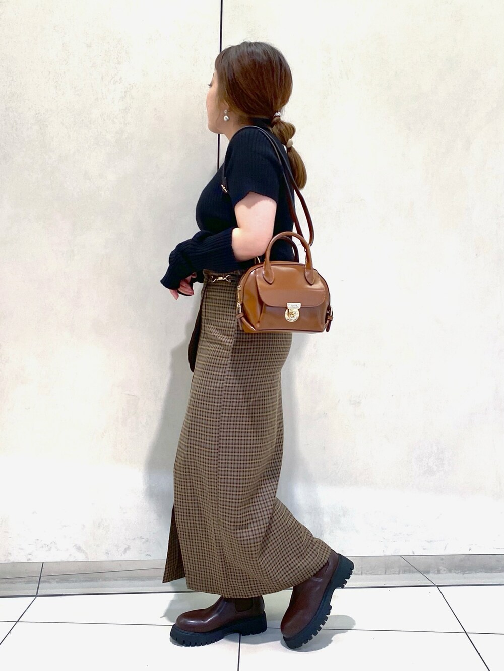 ブラック系のニット/セーター、ブラウン系のスカート、イエロー系のショルダーバッグを着用したレディースの夏コーディネートの2枚目の写真