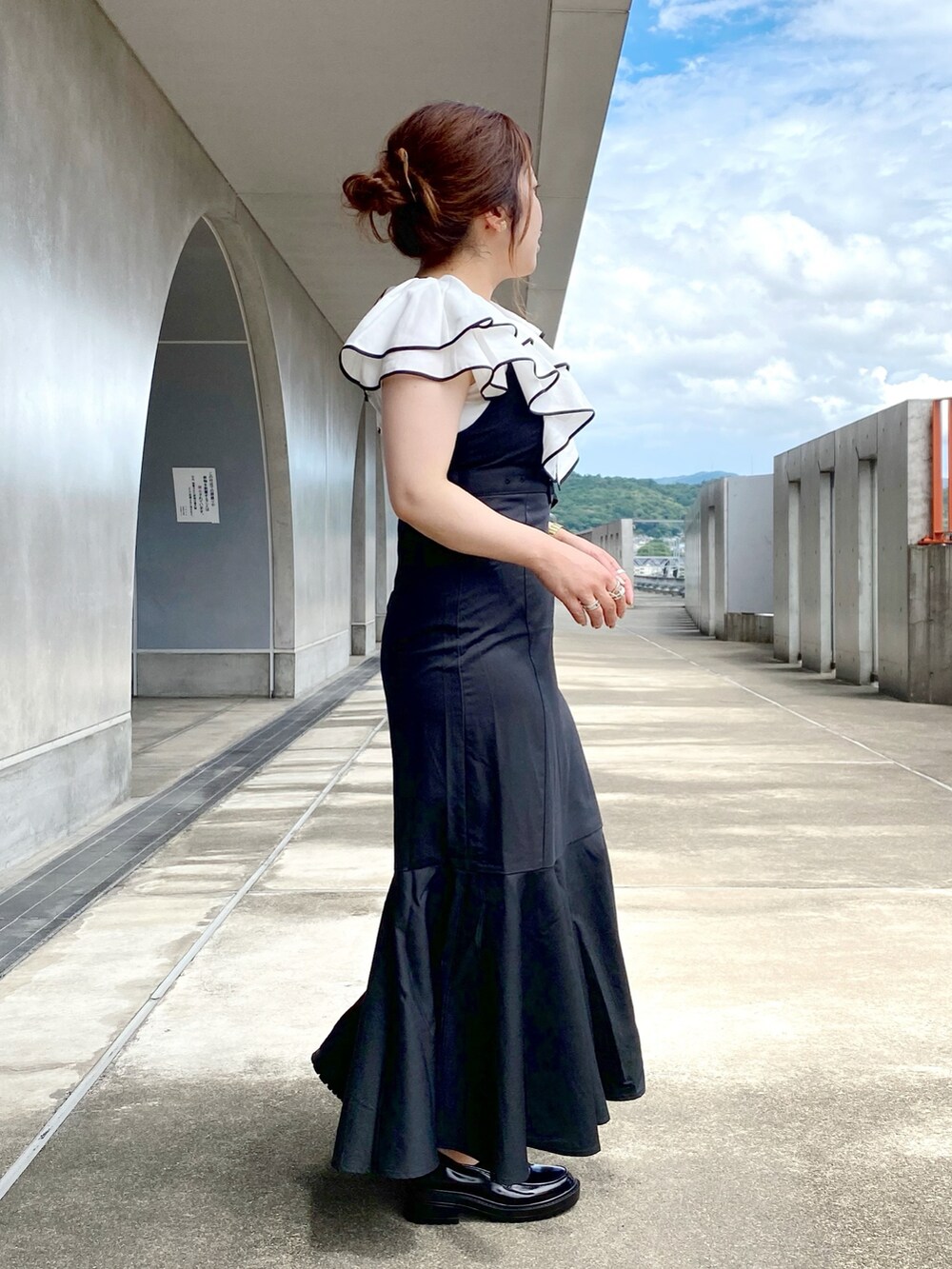 ブラック系のジャンパースカート、ホワイト系のシャツ/ブラウス、ブラック系のローファーを着用したレディースの夏コーディネートの2枚目の写真