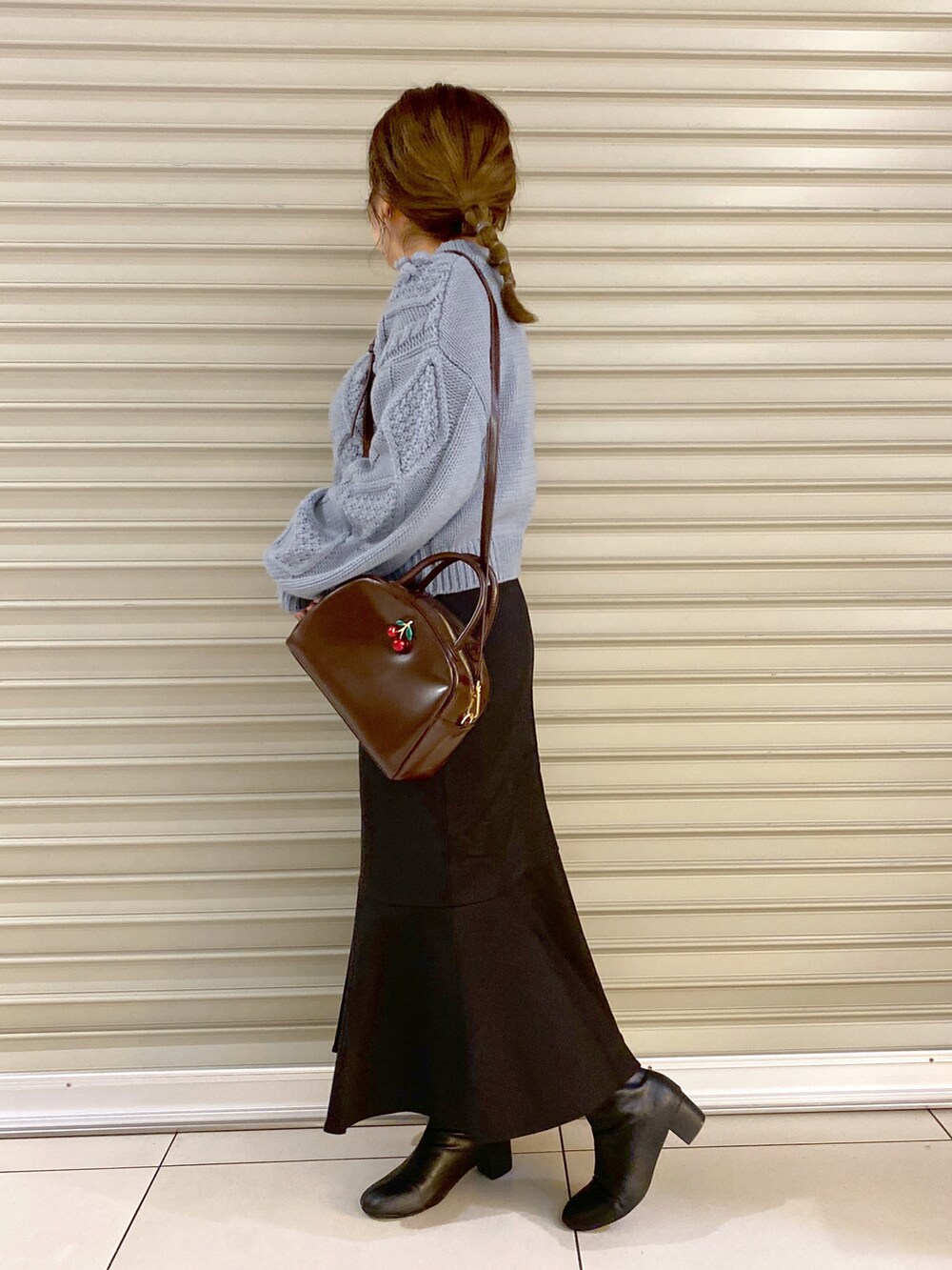 ブルー系のニット/セーター、ブラウン系のショルダーバッグ、ブラック系のスカートを着用したレディースの秋コーディネートの2枚目の写真