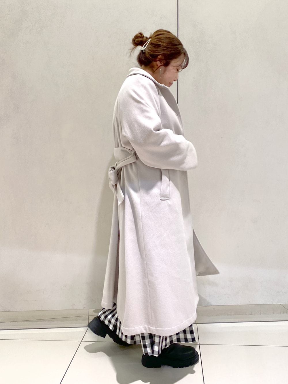 グレー系のステンカラーコート、ホワイト系のニット/セーター、ブラック系のブーツを着用したレディースの冬コーディネートの2枚目の写真