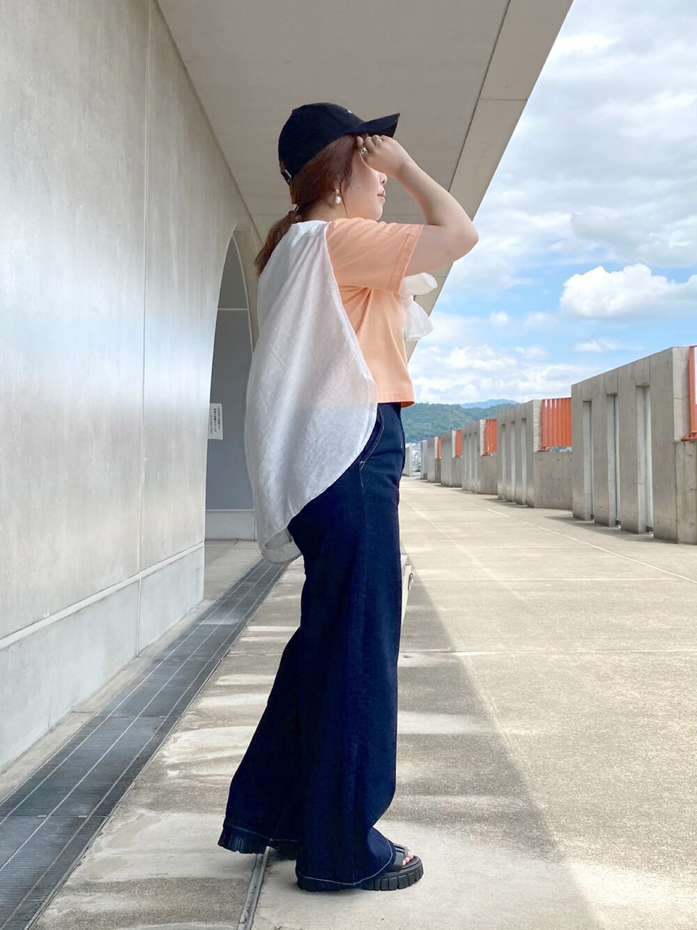 オレンジ系のTシャツ/カットソー、ホワイト系のショルダーバッグ、ブルー系のデニムパンツを着用したレディースの夏コーディネートの3枚目の写真