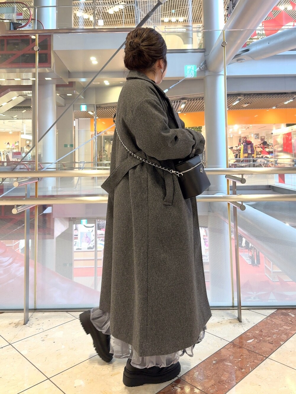 グレー系のステンカラーコート、ブラック系のニット/セーター、グレー系のスカートを着用したレディースの冬コーディネートの3枚目の写真