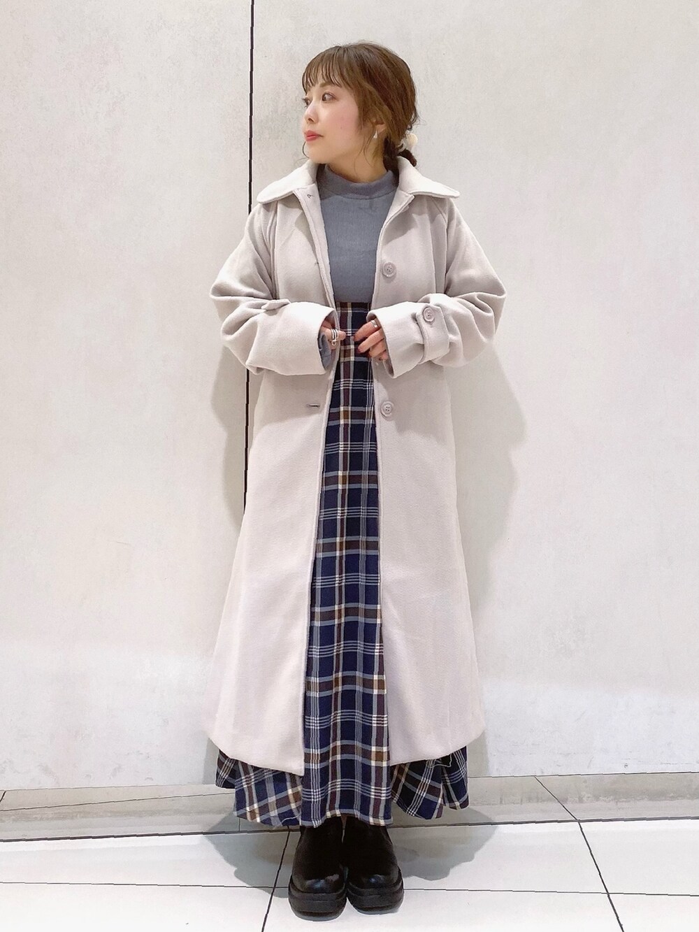 グレー系のワンピース、ホワイト系のステンカラーコート、ブラック系のブーツを着用したレディースの冬コーディネートの3枚目の写真