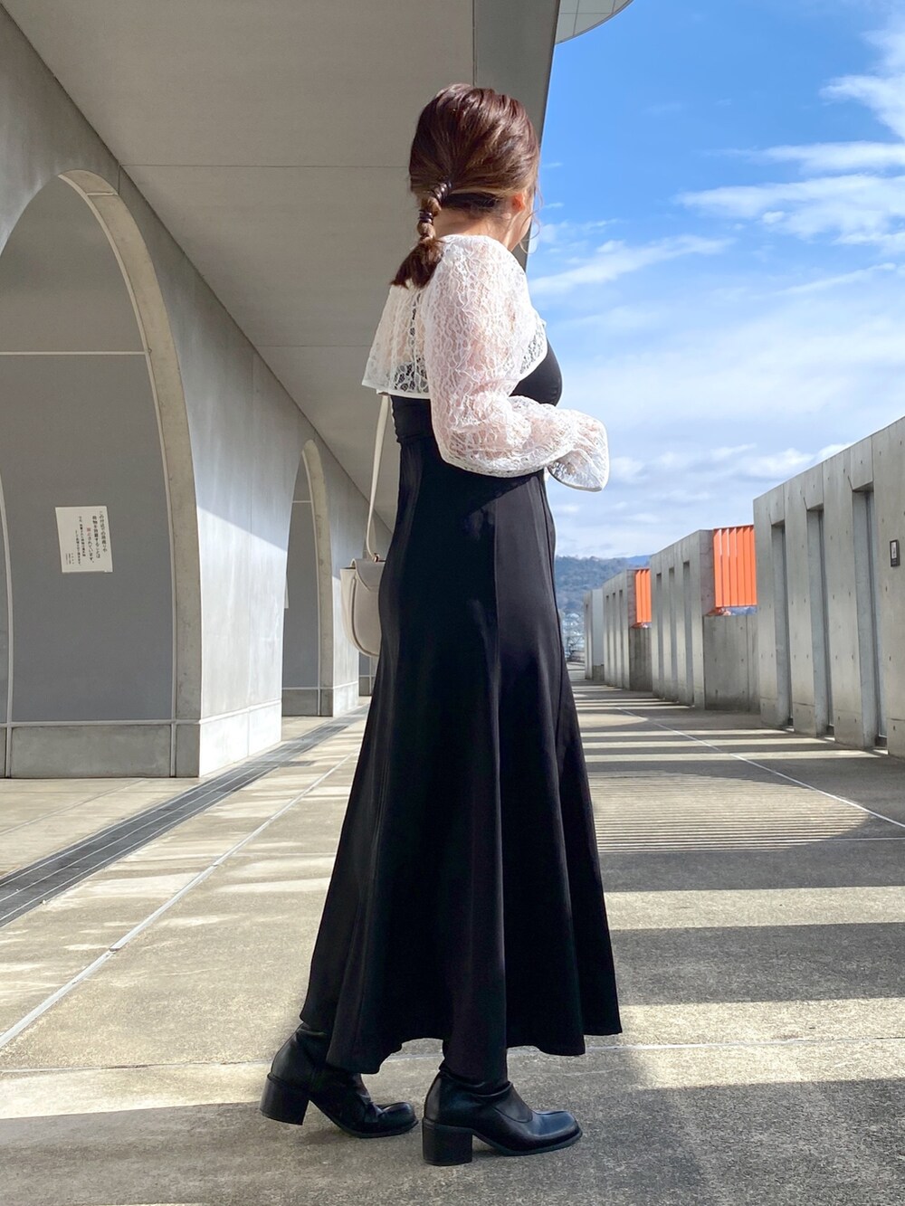 ブラック系のワンピース、ブラック系のブーツ、ホワイト系のショルダーバッグを着用したレディースの冬コーディネートの3枚目の写真