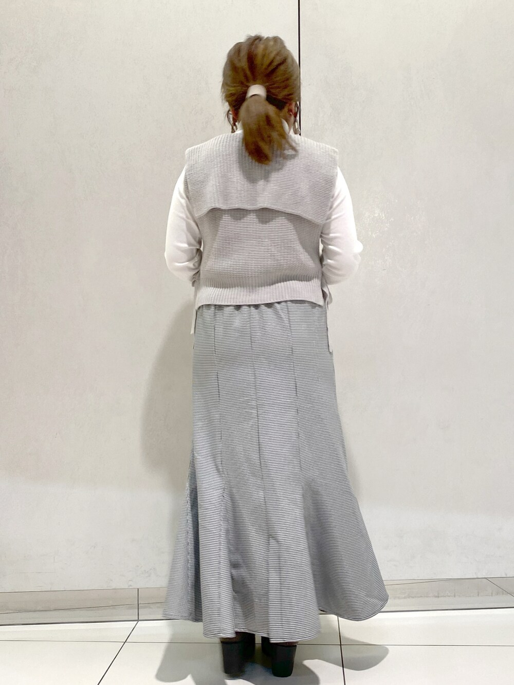 グレー系のベスト、グレー系のショルダーバッグ、ブラック系のスカートを着用したレディースの冬コーディネートの2枚目の写真