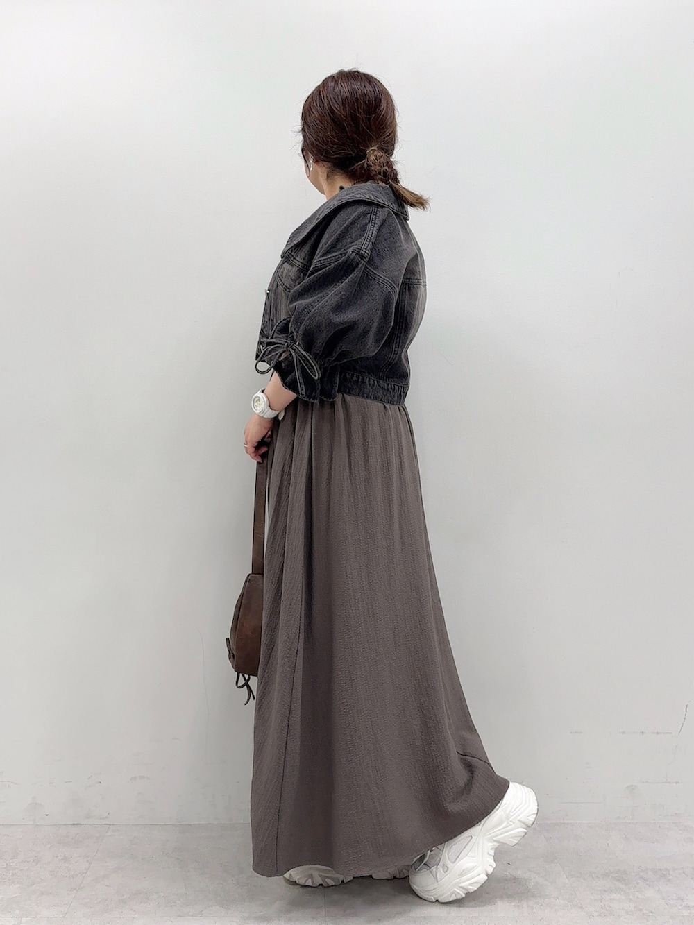 ブラック系のデニムジャケット、ブラウン系のショルダーバッグ、ホワイト系のスニーカーを着用したレディースの夏コーディネートの3枚目の写真