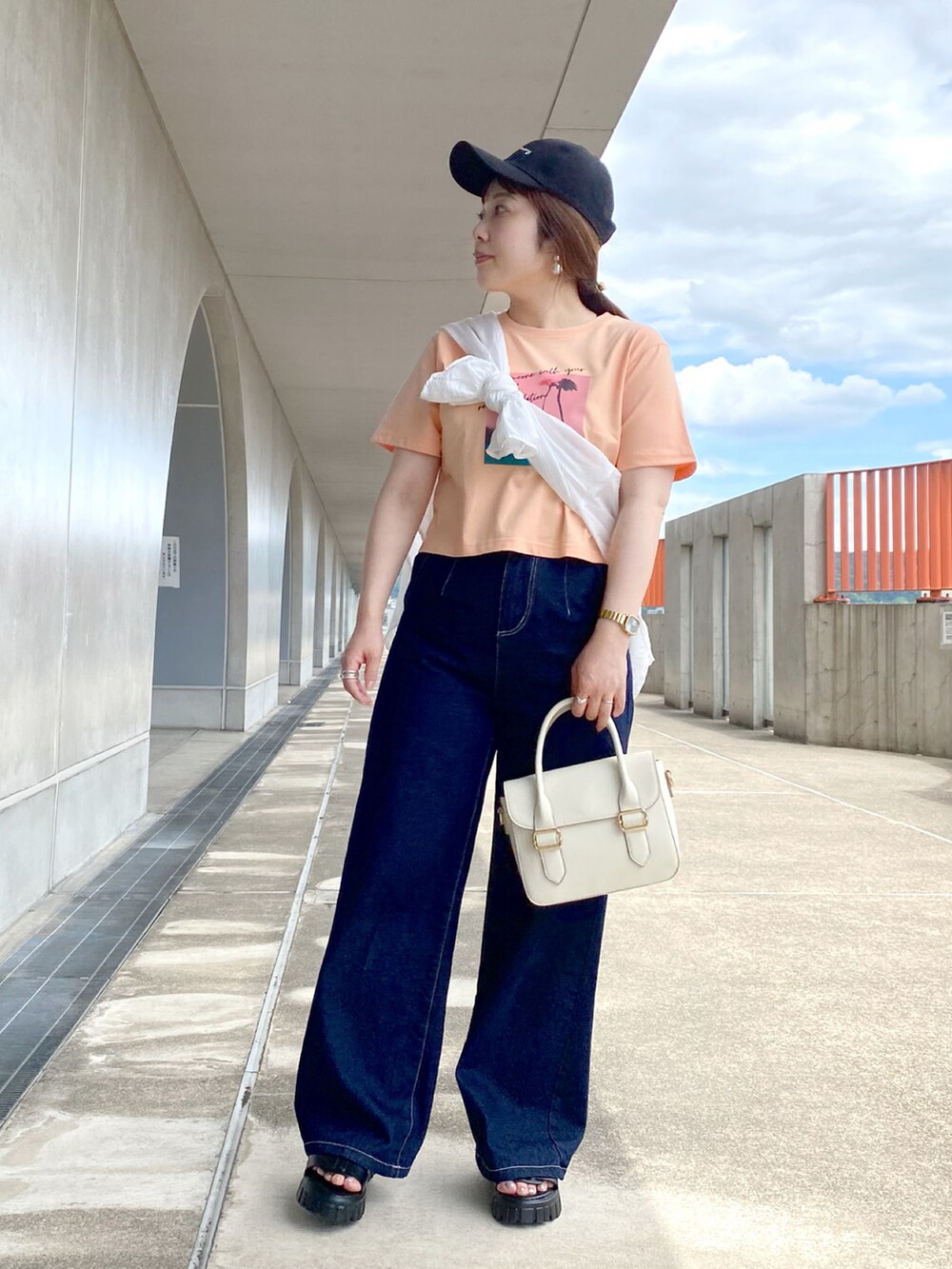 オレンジ系のTシャツ/カットソー、ホワイト系のショルダーバッグ、ブルー系のデニムパンツを着用したレディースの夏コーディネートの2枚目の写真