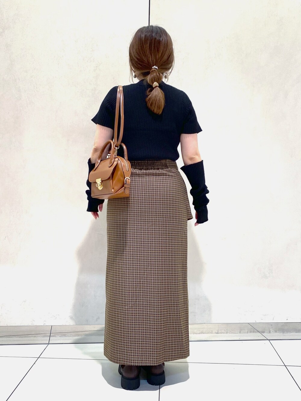 ブラック系のニット/セーター、ブラウン系のスカート、イエロー系のショルダーバッグを着用したレディースの夏コーディネートの3枚目の写真
