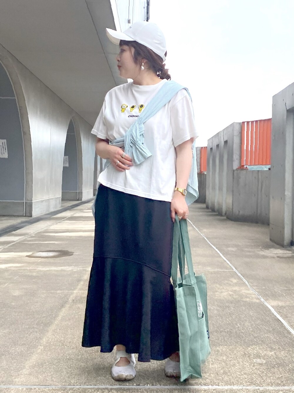 イエロー系のTシャツ/カットソー、ブラック系のスカート、ベージュ系のスニーカーを着用したレディースの夏コーディネートの2枚目の写真