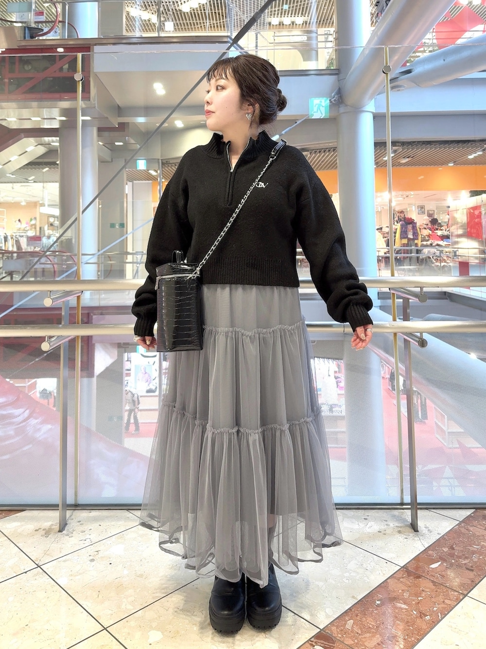 グレー系のステンカラーコート、ブラック系のニット/セーター、グレー系のスカートを着用したレディースの冬コーディネートの2枚目の写真