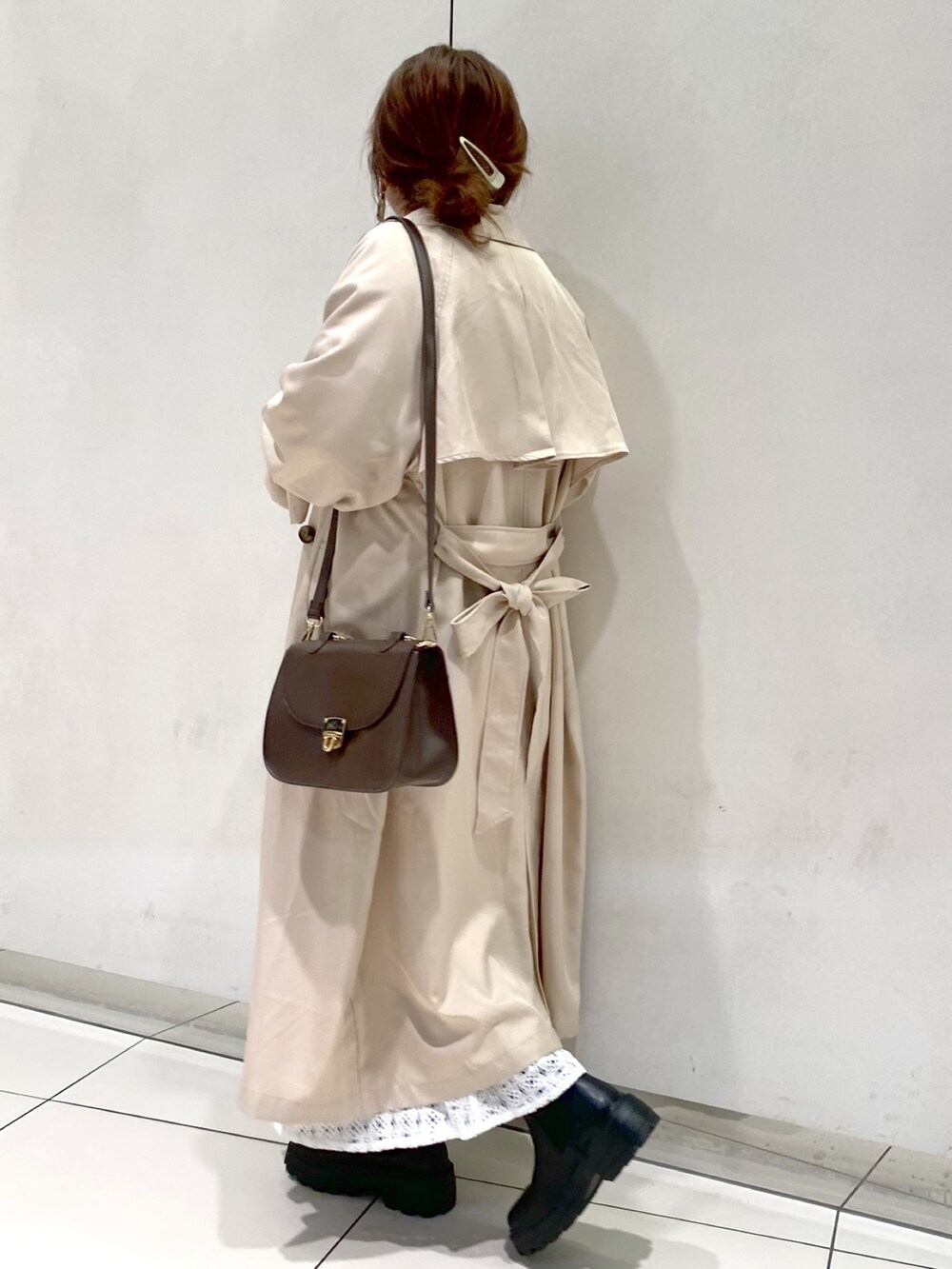 ベージュ系のトレンチコート、ブラウン系のショルダーバッグ、グリーン系のTシャツ/カットソーを着用したレディースの冬コーディネートの2枚目の写真