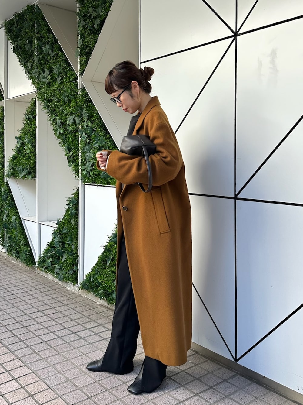 イエロー系のチェスターコート、ブラック系のスラックス、ブラック系のブーツを着用したレディースの秋コーディネートの4枚目の写真