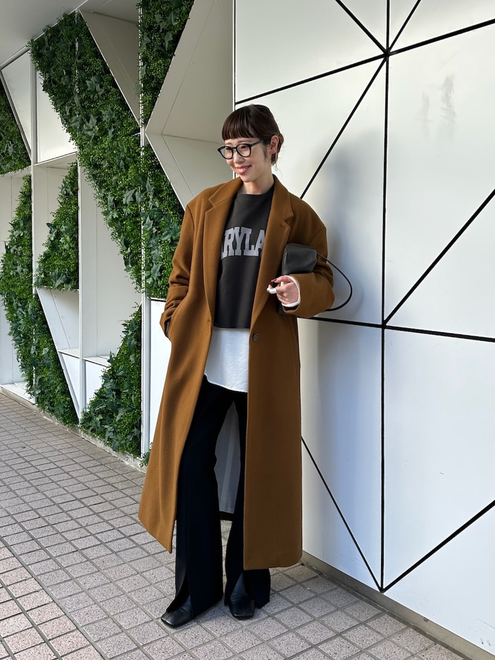 イエロー系のチェスターコート、ブラック系のスラックス、ブラック系のブーツを着用したレディースの秋コーディネートの2枚目の写真