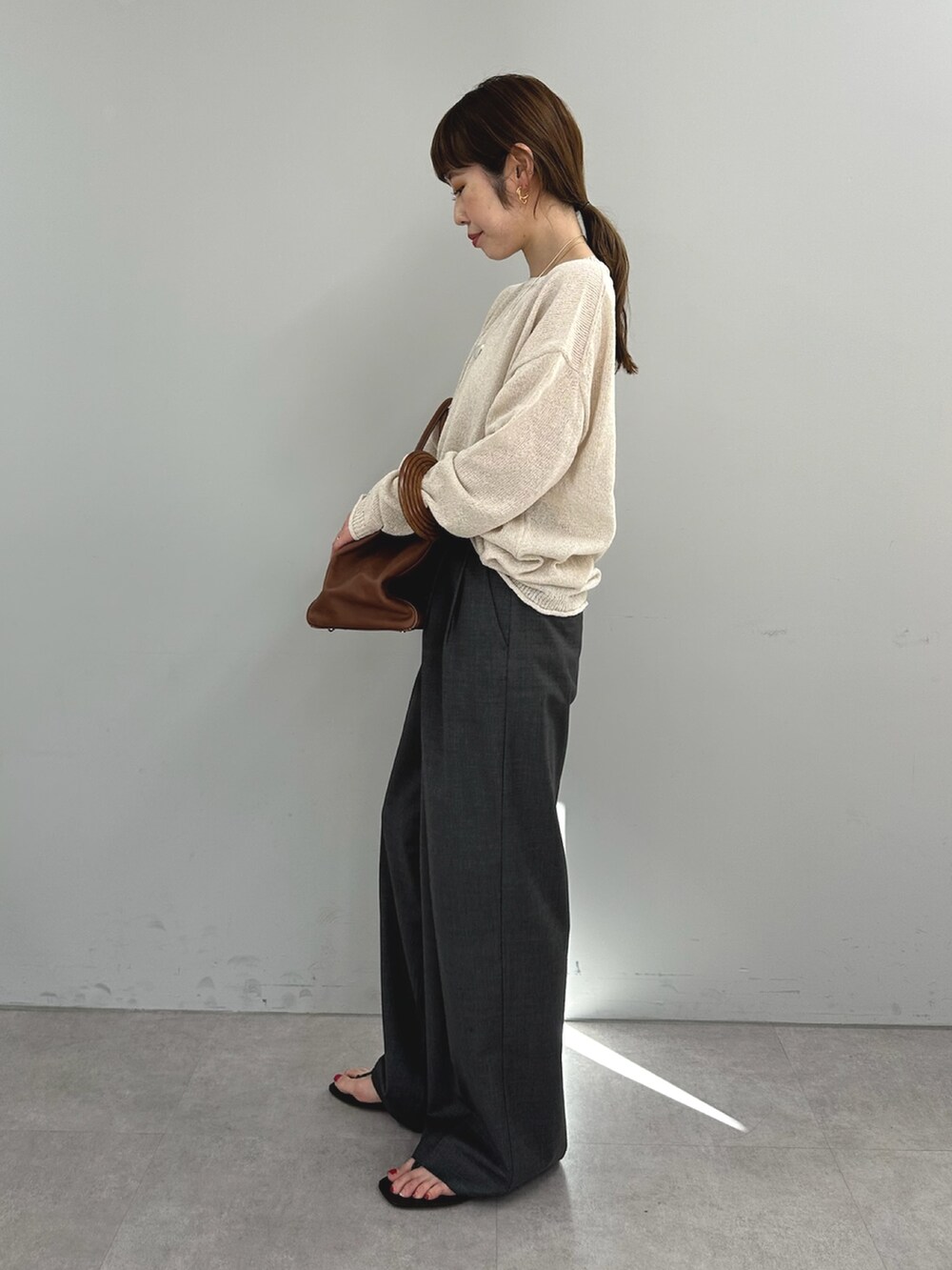 グレー系のスラックス、イエロー系のボストンバッグ、ベージュ系のニット/セーターを着用したレディースの春コーディネートの4枚目の写真