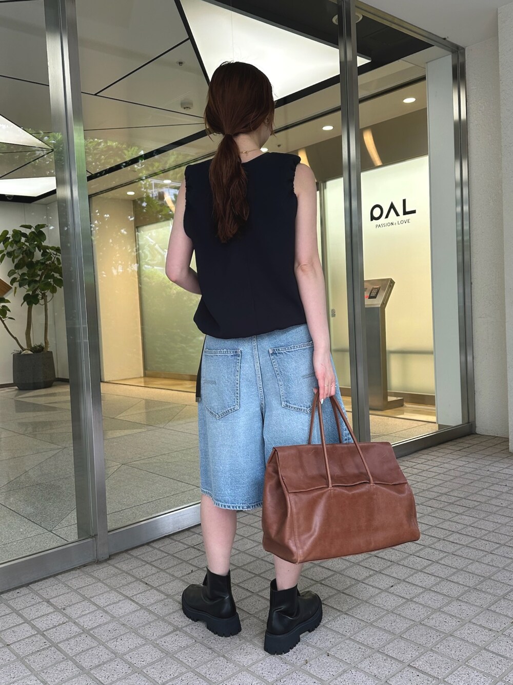 ブルー系のデニムパンツ、ブラック系のブーツ、イエロー系のボストンバッグを着用したレディースの夏コーディネートの3枚目の写真