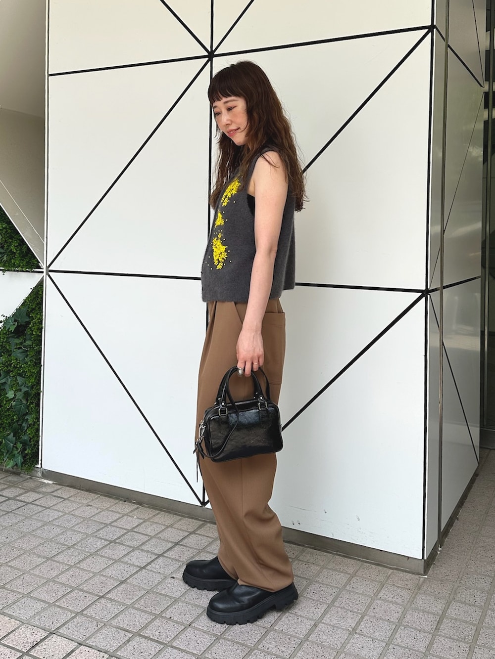 グレー系のベスト、ブラック系のハンドバッグ、ブラック系のブーツを着用したレディースの夏コーディネートの2枚目の写真