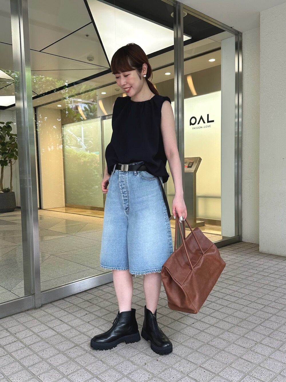 ブルー系のデニムパンツ、ブラック系のブーツ、イエロー系のボストンバッグを着用したレディースの夏コーディネートの4枚目の写真