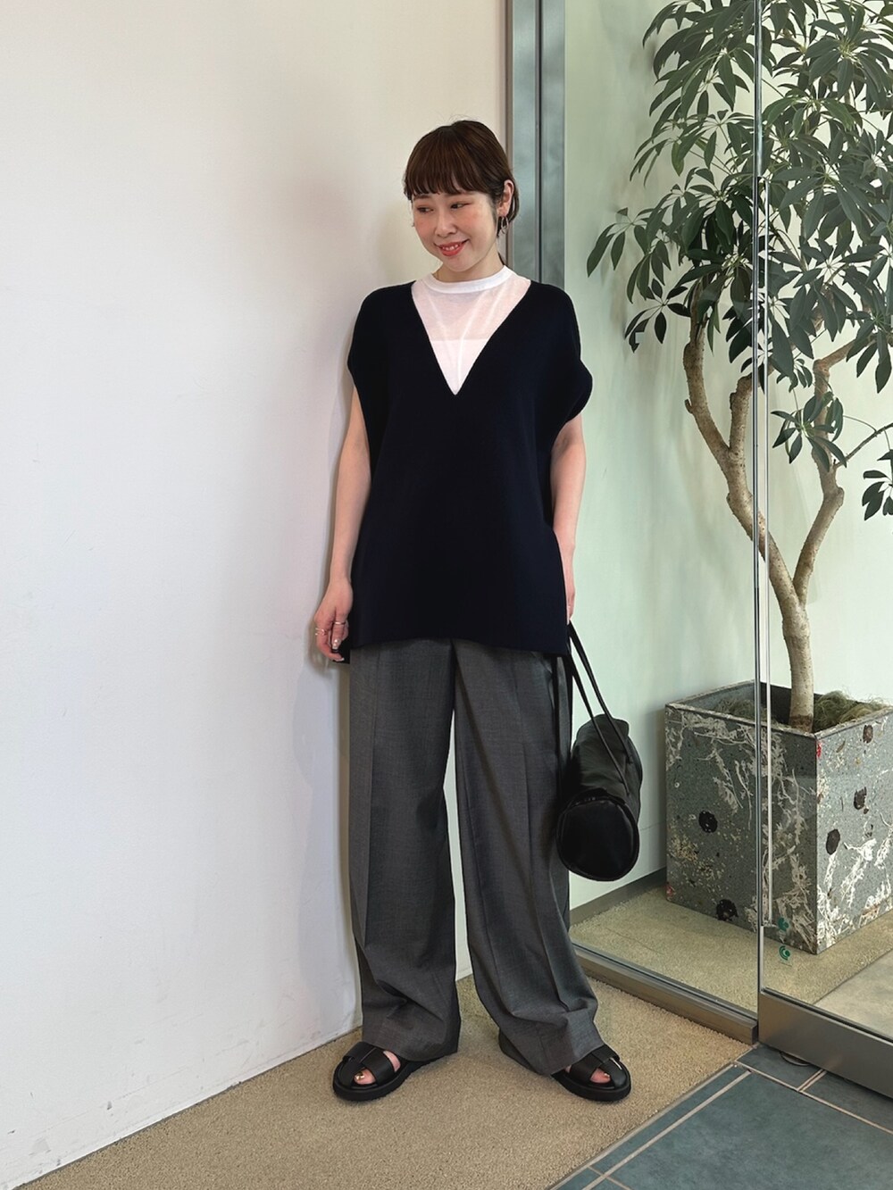 グレー系のスラックス、ホワイト系のハンドバッグ、ブラック系のニット/セーターを着用したレディースの春コーディネートの2枚目の写真