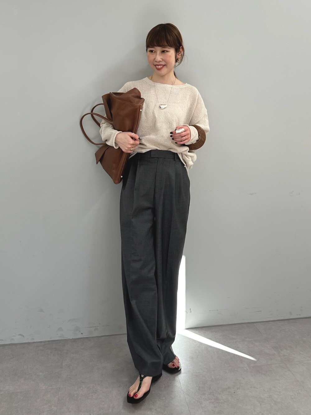 グレー系のスラックス、イエロー系のボストンバッグ、ベージュ系のニット/セーターを着用したレディースの春コーディネートの3枚目の写真