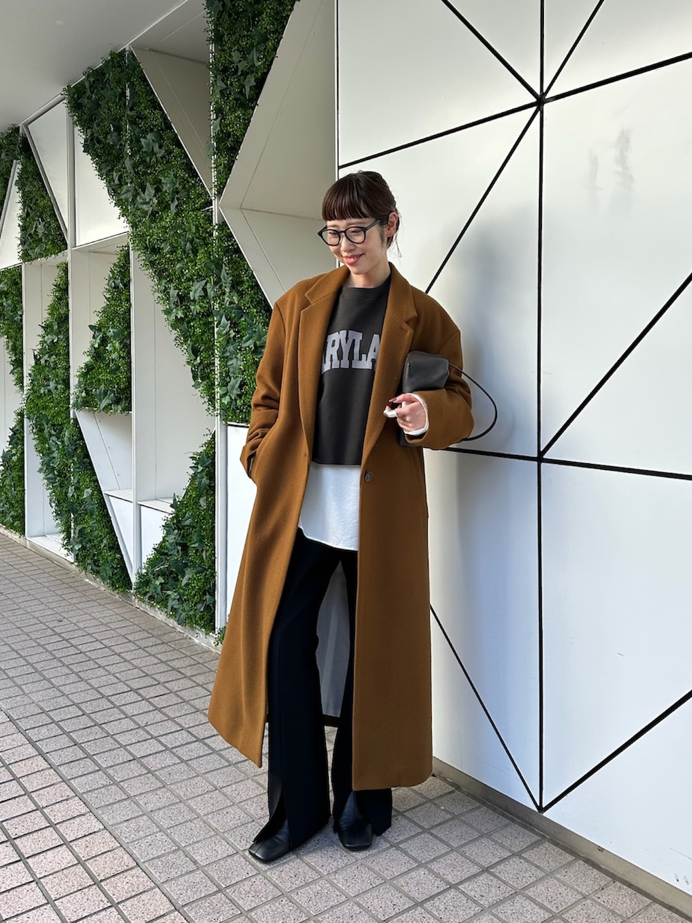 イエロー系のチェスターコート、ブラック系のスラックス、ブラック系のブーツを着用したレディースの秋コーディネートの3枚目の写真