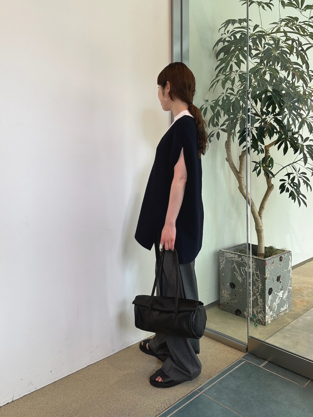 グレー系のスラックス、ホワイト系のハンドバッグ、ブラック系のニット/セーターを着用したレディースの春コーディネートの3枚目の写真