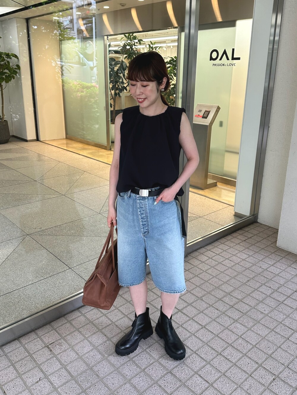 ブルー系のデニムパンツ、ブラック系のブーツ、イエロー系のボストンバッグを着用したレディースの夏コーディネートの2枚目の写真