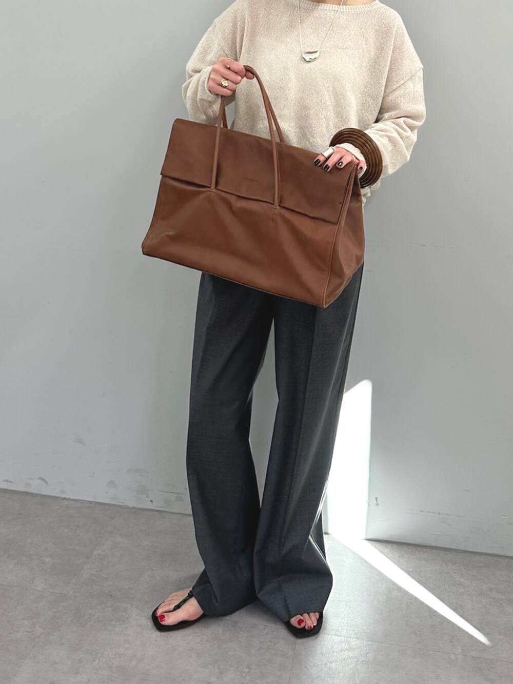 グレー系のスラックス、イエロー系のボストンバッグ、ベージュ系のニット/セーターを着用したレディースの春コーディネートの6枚目の写真