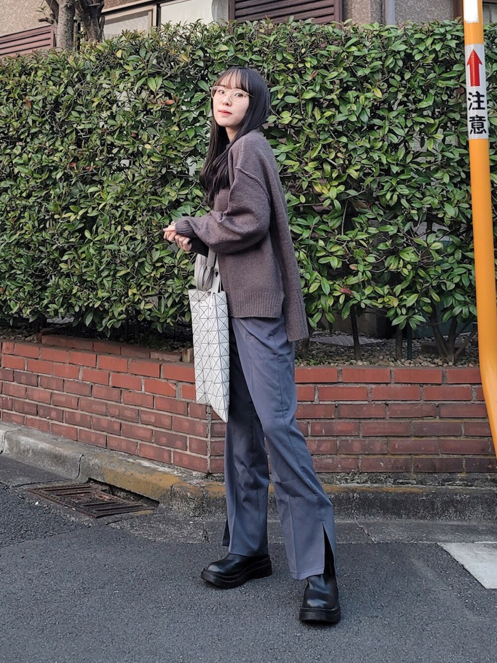 グレー系のニット/セーター、グレー系のスラックス、ホワイト系のトートバッグを着用したレディースの冬コーディネートの2枚目の写真