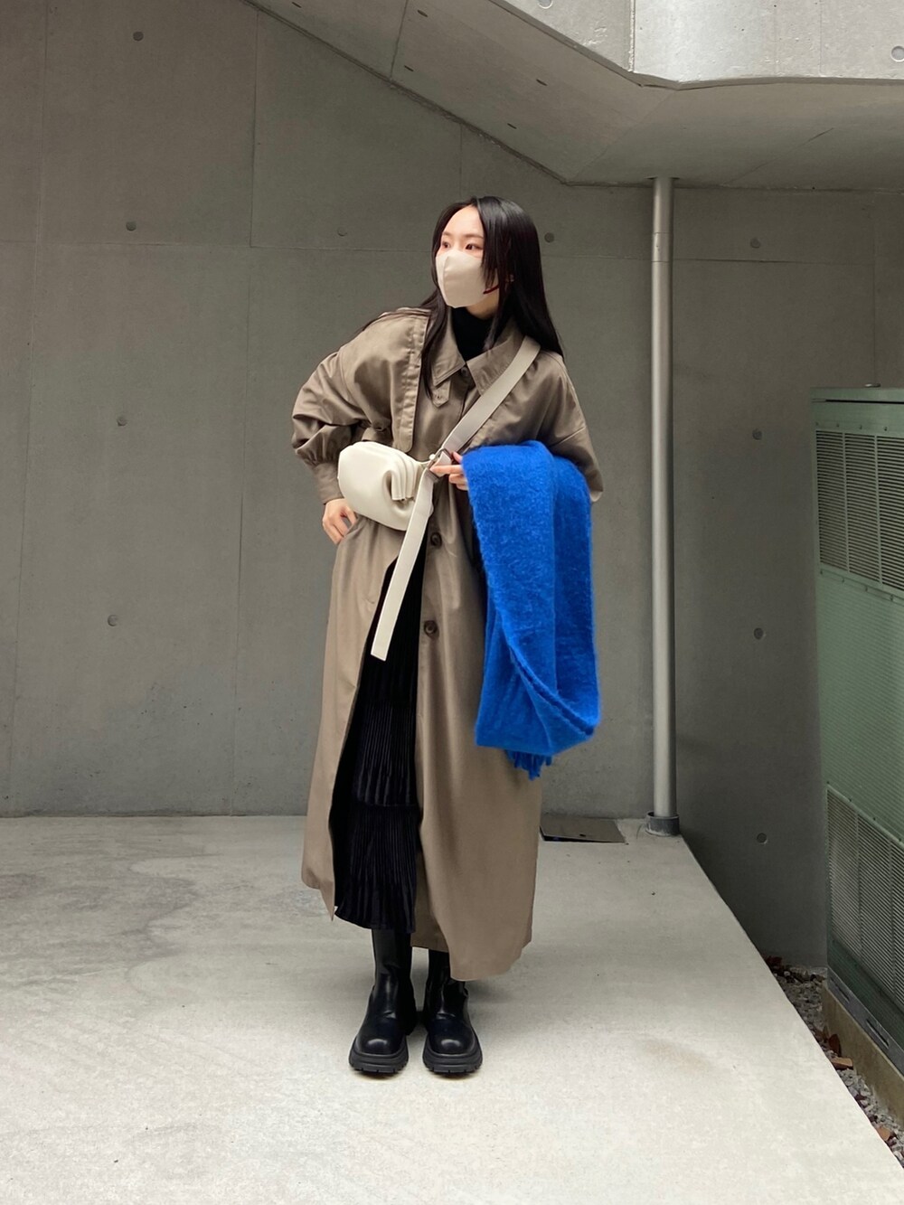 グレー系のトレンチコート、ホワイト系のバッグ、ブラック系のブーツを着用したレディースの秋コーディネートの2枚目の写真