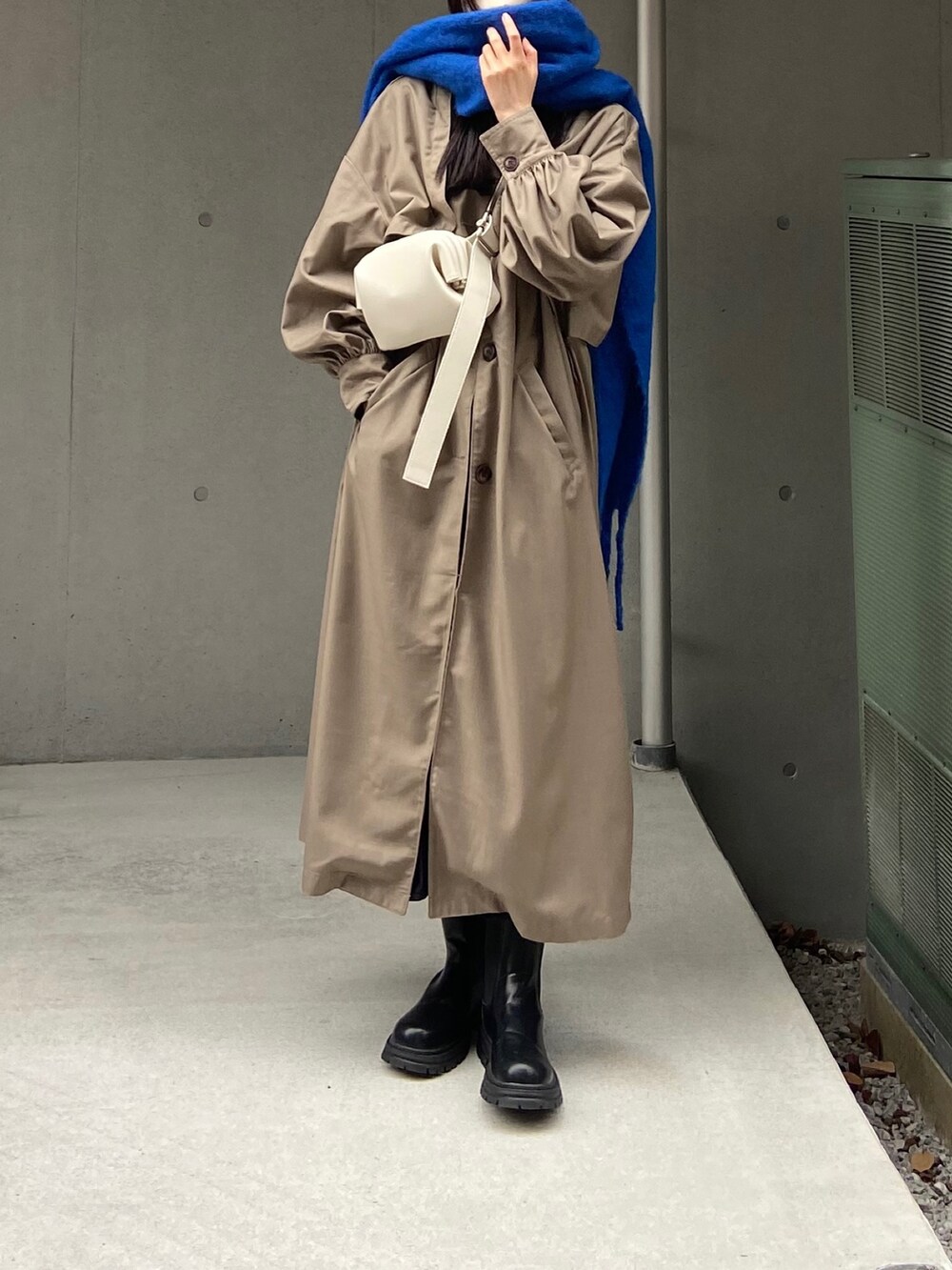 グレー系のトレンチコート、ホワイト系のバッグ、ブラック系のブーツを着用したレディースの秋コーディネートの4枚目の写真