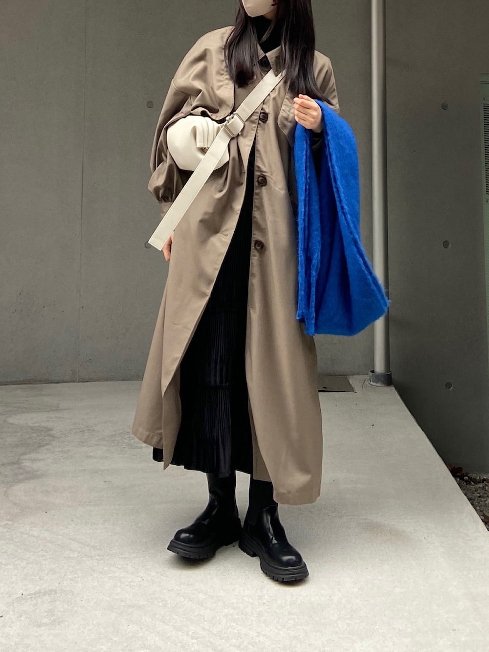 グレー系のトレンチコート、ホワイト系のバッグ、ブラック系のブーツを着用したレディースの秋コーディネートの3枚目の写真