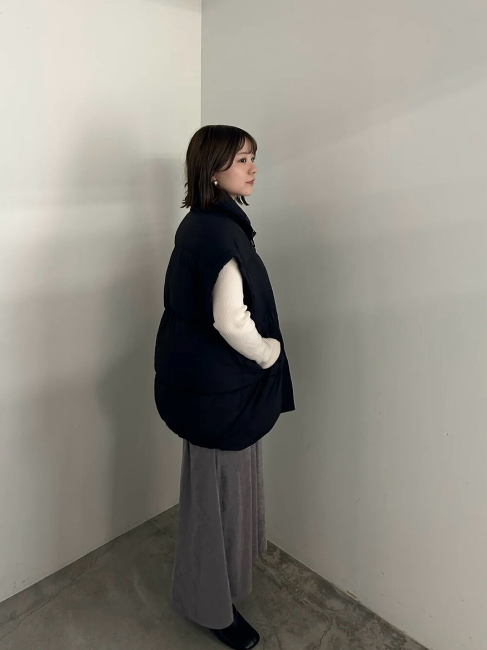 ブラック系のダウンベスト、ホワイト系のニット/セーター、グレー系のスカートを着用したレディースの秋コーディネートの2枚目の写真